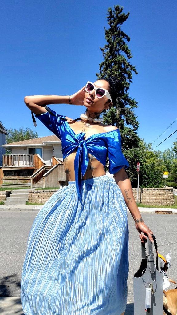 A woman in a blue top and skirt is walking down the street, wearing a baby blue 2-piece outfit.