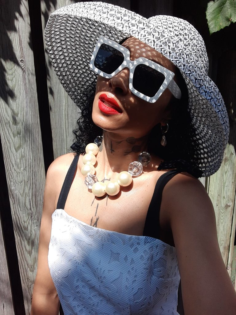 Elegant woman in Audrey Hepburn wide brimmed mesh hat and oversized sunglasses, with red lipstick.